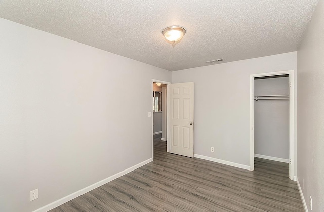 unfurnished bedroom with visible vents, a textured ceiling, wood finished floors, a closet, and baseboards