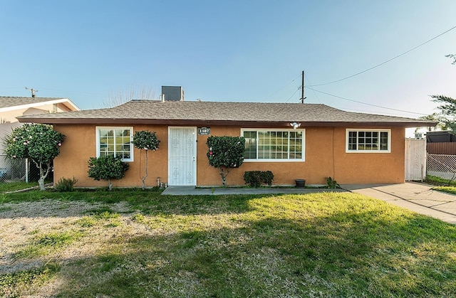 single story home with stucco siding, roof with shingles, a front lawn, and fence