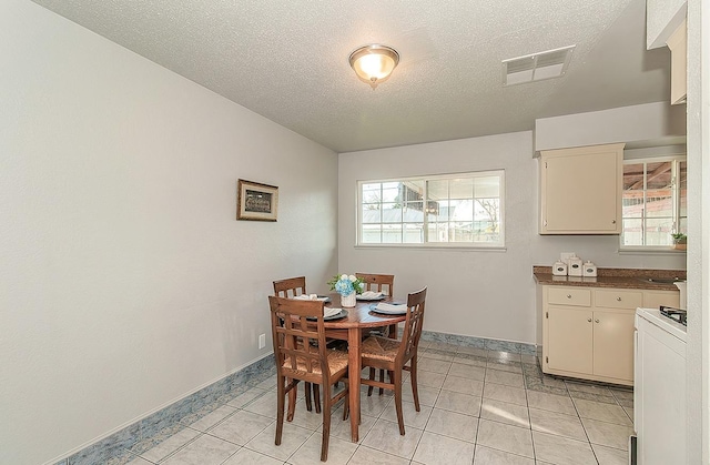 dining area featuring light tile patterned flooring, visible vents, a textured ceiling, and baseboards