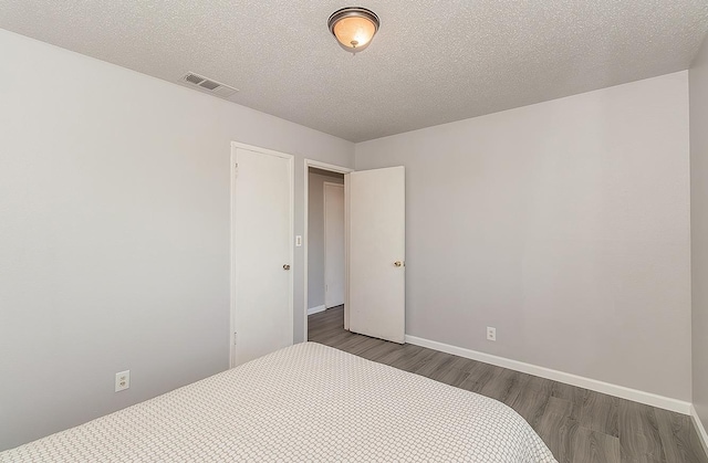 bedroom with visible vents, baseboards, a textured ceiling, and wood finished floors