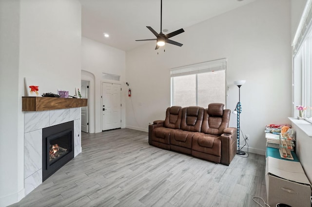 living room with a tiled fireplace, light wood-style flooring, baseboards, and a towering ceiling