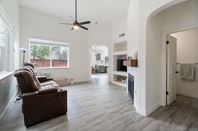 living room featuring light wood-type flooring, visible vents, built in features, arched walkways, and a towering ceiling