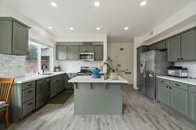 kitchen featuring a kitchen island, a sink, stainless steel appliances, light countertops, and light wood-style floors