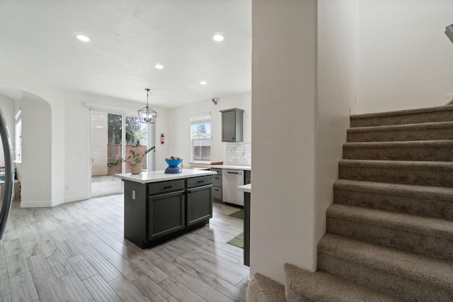 kitchen featuring light wood-style flooring, arched walkways, light countertops, dishwasher, and backsplash