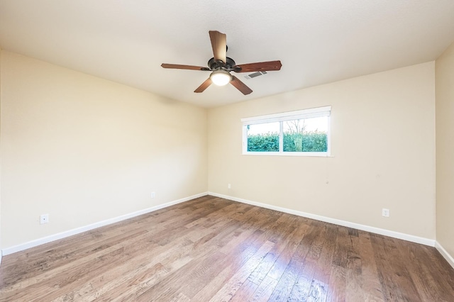 spare room featuring ceiling fan, visible vents, baseboards, and wood finished floors