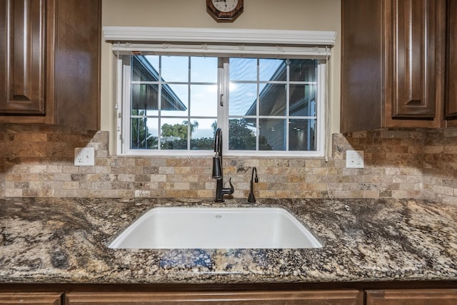 details featuring dark brown cabinetry, tasteful backsplash, dark stone counters, and a sink