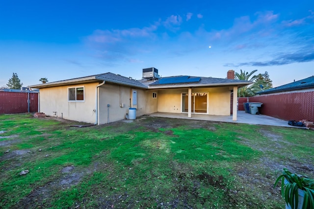 rear view of property featuring central air condition unit, roof mounted solar panels, stucco siding, a fenced backyard, and a patio