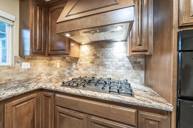 kitchen featuring decorative backsplash, gas cooktop, light stone countertops, and premium range hood