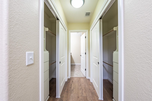 hall with visible vents, baseboards, wood finished floors, and a textured wall