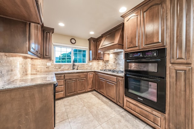 kitchen with premium range hood, dobule oven black, a sink, light stone countertops, and stainless steel gas cooktop