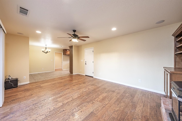 unfurnished living room with visible vents, baseboards, light wood-type flooring, ceiling fan with notable chandelier, and a textured ceiling