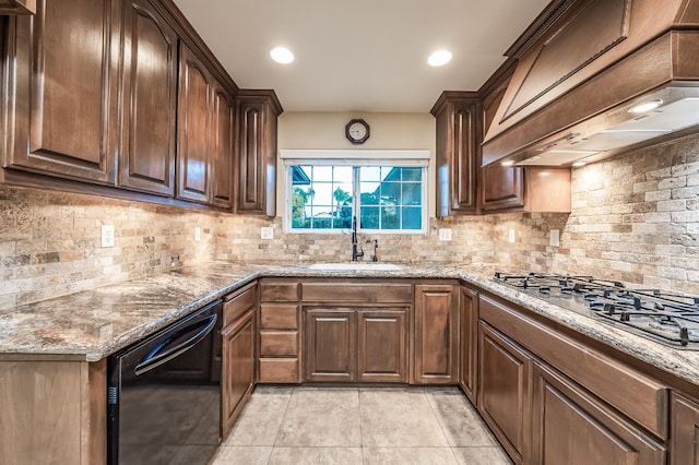 kitchen with light stone countertops, premium range hood, stainless steel gas cooktop, a sink, and black dishwasher