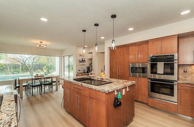 kitchen with light stone counters, backsplash, a kitchen island, stainless steel appliances, and brown cabinetry