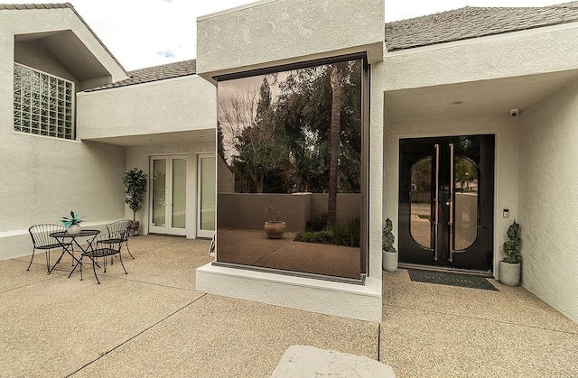 view of exterior entry featuring a patio area, french doors, roof with shingles, and stucco siding