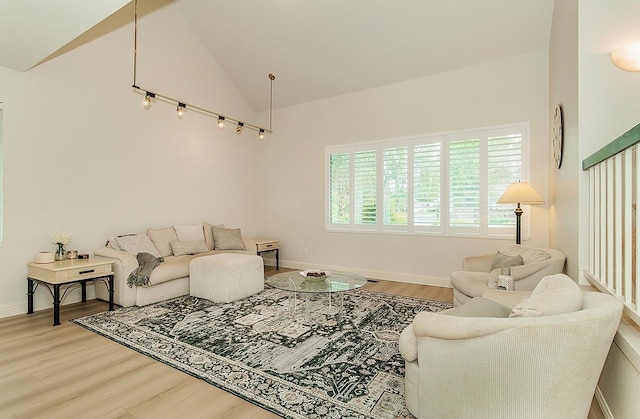 living area with baseboards, high vaulted ceiling, and light wood finished floors