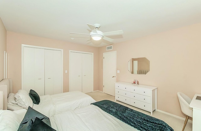 bedroom featuring visible vents, two closets, baseboards, ceiling fan, and light carpet