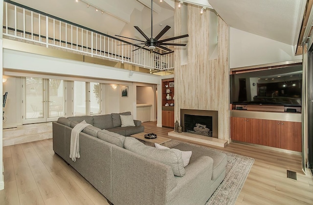 living room featuring visible vents, a large fireplace, light wood-style floors, high vaulted ceiling, and a ceiling fan