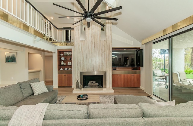 living area with ceiling fan, high vaulted ceiling, wood finished floors, and a large fireplace