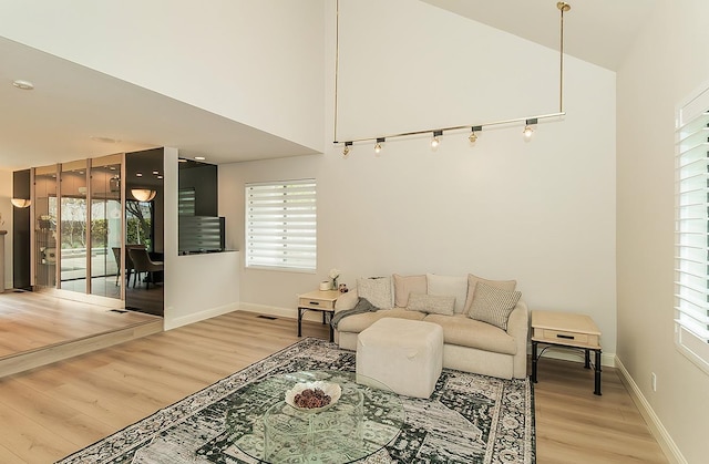 living room with visible vents, light wood-style floors, baseboards, and high vaulted ceiling