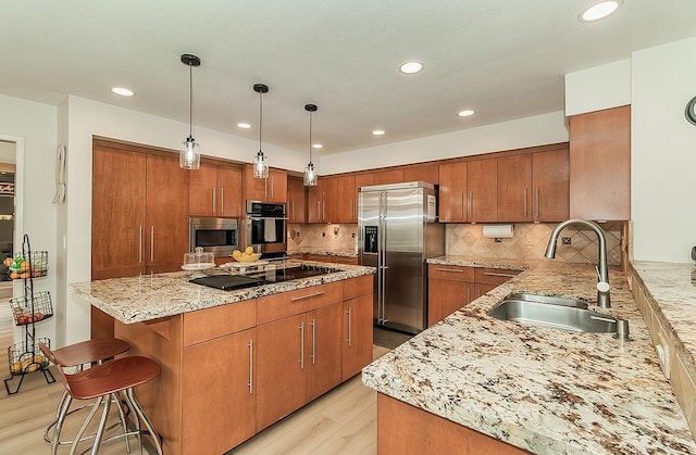 kitchen featuring brown cabinetry, light stone countertops, a sink, stainless steel appliances, and a center island