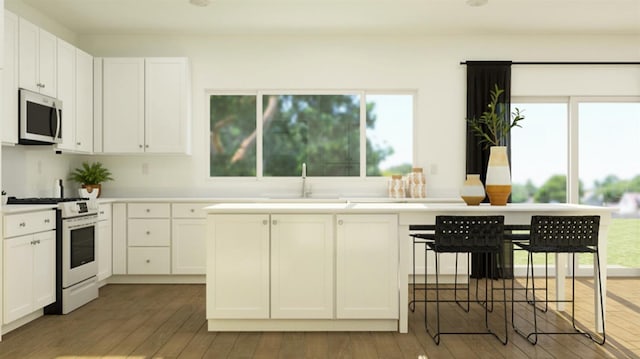 kitchen with stainless steel microwave, white cabinetry, white range with gas stovetop, and hardwood / wood-style flooring