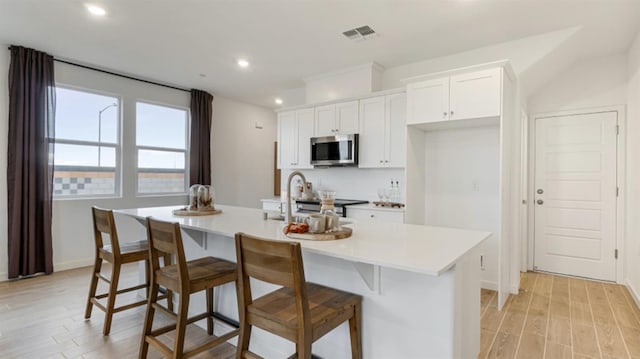 kitchen featuring stainless steel microwave, visible vents, light wood-style floors, white cabinets, and a sink