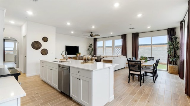 kitchen featuring a sink, wood tiled floor, dishwasher, arched walkways, and a kitchen island with sink