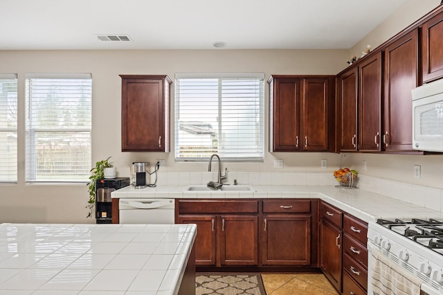 kitchen featuring visible vents, a sink, tile countertops, white appliances, and a healthy amount of sunlight