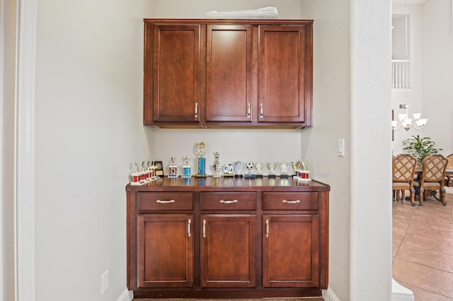 bar with a notable chandelier, light tile patterned flooring, and baseboards