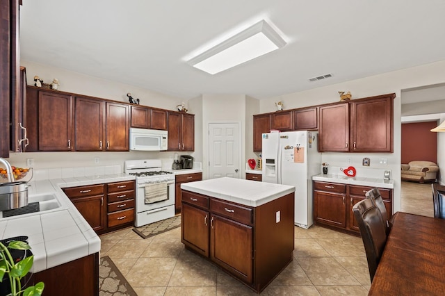 kitchen featuring visible vents, a sink, a center island, tile countertops, and white appliances