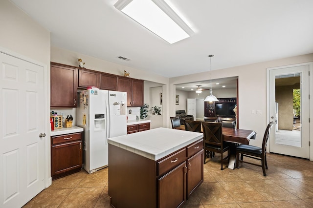 kitchen with visible vents, hanging light fixtures, tile counters, white fridge with ice dispenser, and a center island