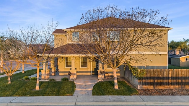 view of front of house with stucco siding, a porch, a front lawn, and fence