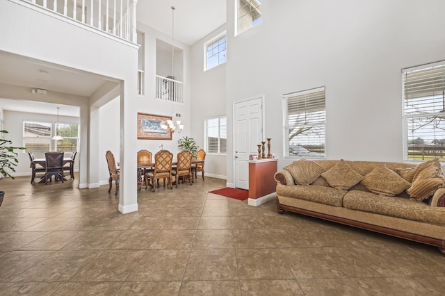 living area with a healthy amount of sunlight, baseboards, a high ceiling, and an inviting chandelier