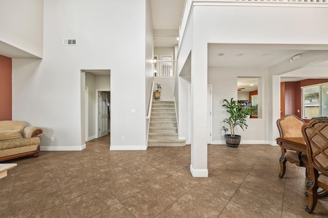 tiled foyer entrance featuring stairway, baseboards, visible vents, and a towering ceiling