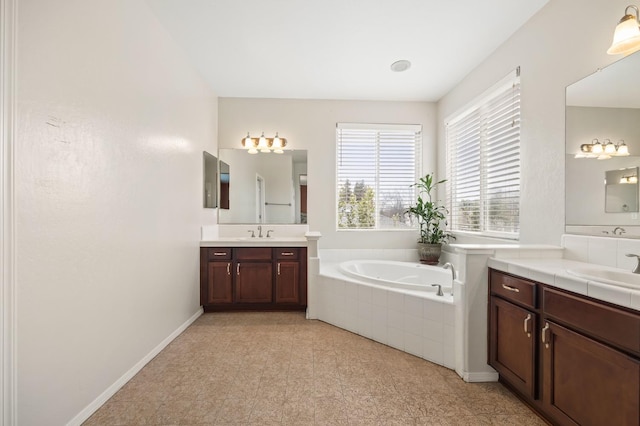 full bath with two vanities, a bath, baseboards, and a sink