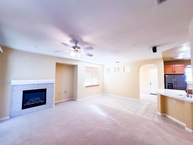 unfurnished living room featuring a ceiling fan, light tile patterned floors, light colored carpet, and arched walkways