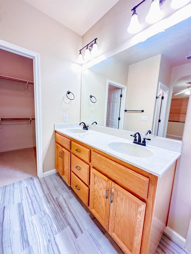 full bathroom with double vanity, a spacious closet, a ceiling fan, and a sink