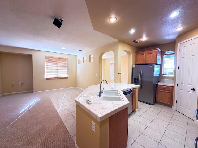 kitchen featuring tile counters, dishwasher, fridge with ice dispenser, light tile patterned floors, and a sink