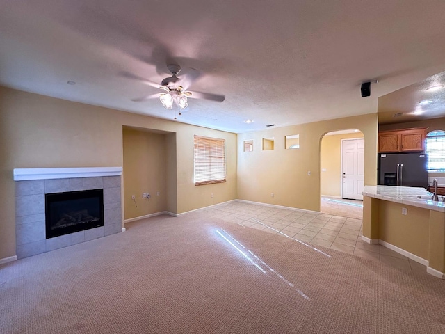 unfurnished living room featuring ceiling fan, light tile patterned floors, a fireplace, arched walkways, and a sink