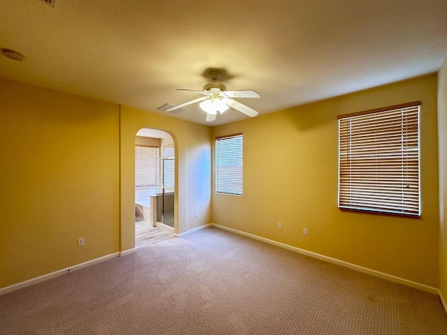 unfurnished room with baseboards, light colored carpet, arched walkways, and ceiling fan