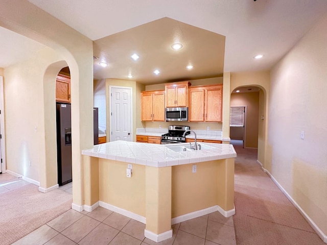 kitchen featuring tile countertops, light carpet, appliances with stainless steel finishes, arched walkways, and a sink