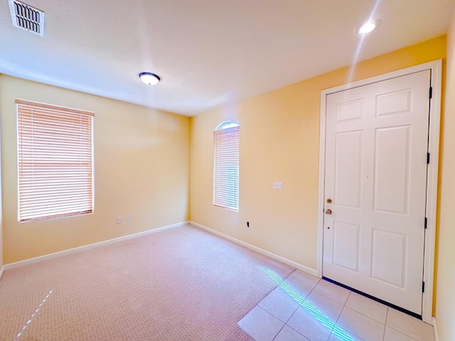 empty room featuring light tile patterned flooring, visible vents, light colored carpet, and baseboards