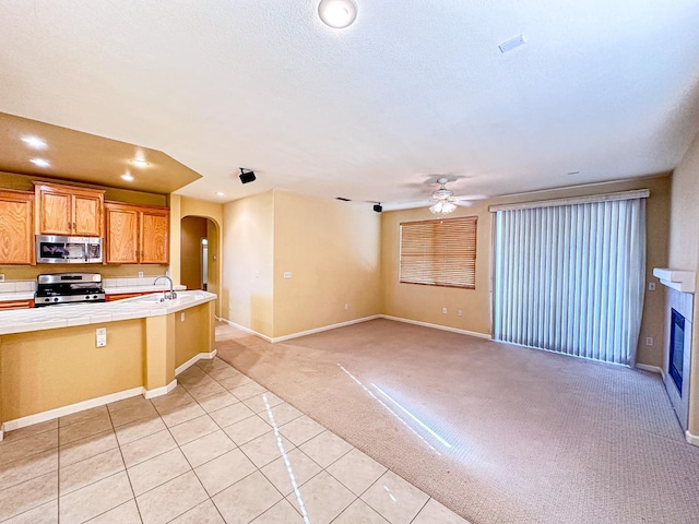 kitchen featuring light carpet, a glass covered fireplace, stainless steel appliances, arched walkways, and tile counters