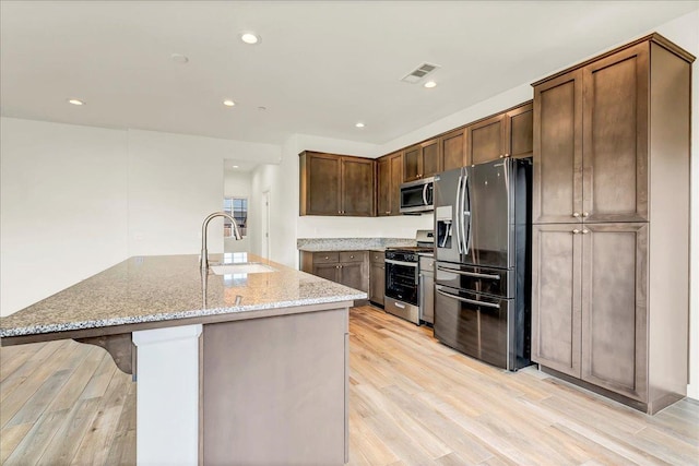 kitchen with light stone counters, stainless steel appliances, light wood-type flooring, and a sink