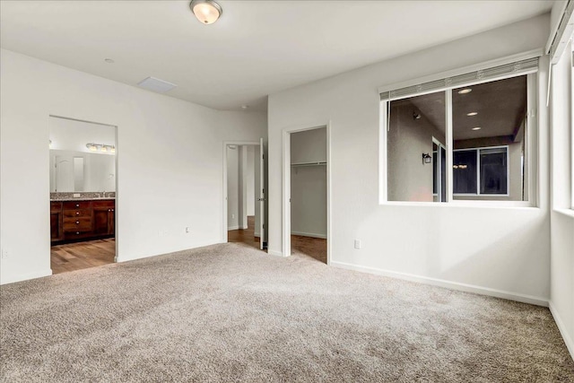 unfurnished bedroom featuring baseboards, ensuite bath, a spacious closet, a closet, and carpet flooring