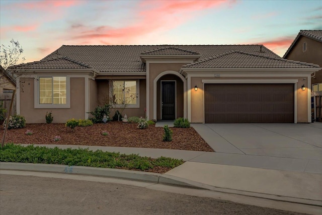 view of front facade with stucco siding, a tiled roof, concrete driveway, and an attached garage