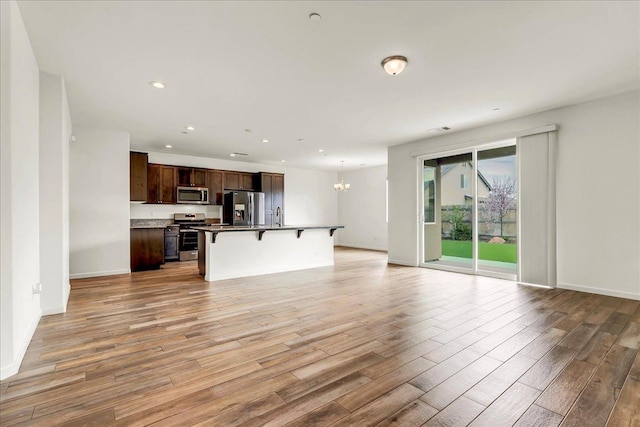 unfurnished living room featuring light wood-type flooring, a sink, recessed lighting, baseboards, and a chandelier