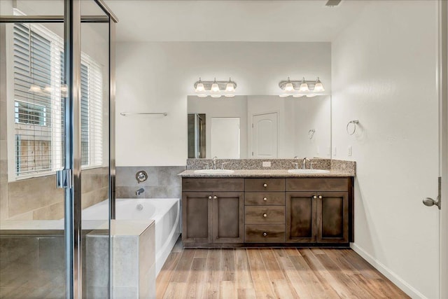 bathroom featuring a garden tub, wood finished floors, double vanity, and a sink