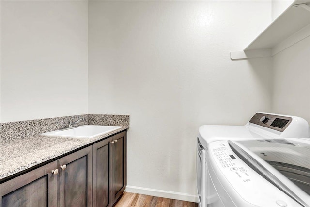 laundry room with washer and dryer, a sink, cabinet space, light wood-style floors, and baseboards