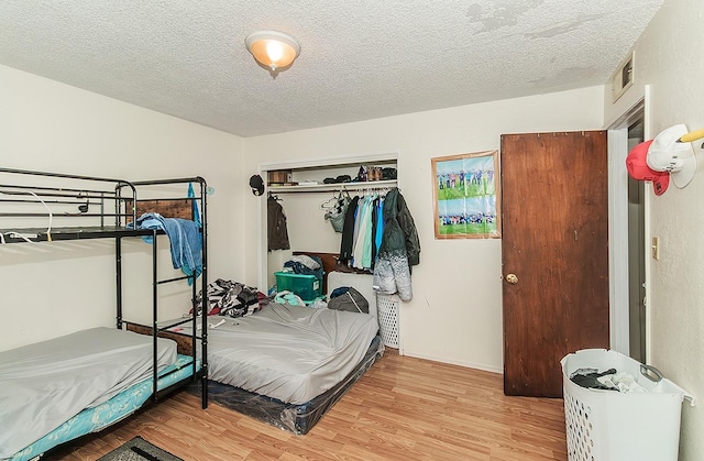 bedroom with a closet, a textured ceiling, visible vents, and wood finished floors